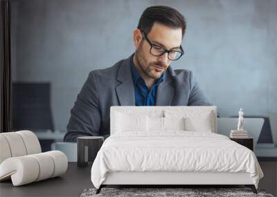 A mid adult Caucasian man in professional attire intently works on his laptop in an office, checking his wristwatch as he manages time efficiently. Wall mural