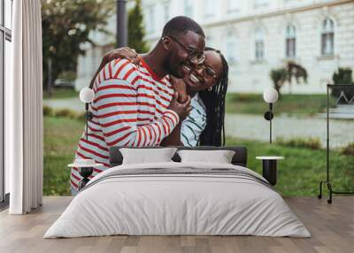 A smiling black couple dressed in casual attire share an embrace on a university campus, displaying affection and connection in an educational setting. Wall mural