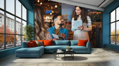 A smiling waitress takes an order from guests at a cozy bar, with one man holding a menu and engaging in lively banter dressed in casual attire. Wall mural