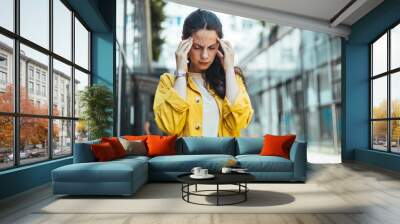 Dizzy woman complaining in the street. Young woman standing suffering for headache at street. Woman standing with eyes closed and head in hands on street Wall mural