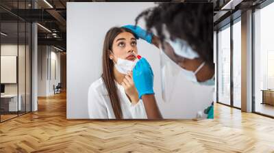 Doctor in protective workwear taking nose swab test from young woman. Close-up of woman having PCR testing at the hospital. Woman being screened for coronavirus in a laboratory Wall mural