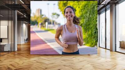 Happy slim woman wearing sportswear jogging in the city at sunrise. Young beautiful female in sports bra running outdoor. Workout exercise in the morning. Healthy and active lifestyle concept. Wall mural