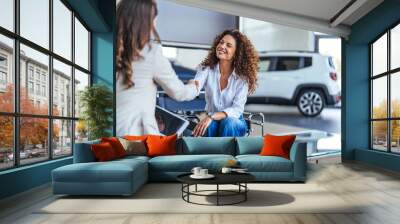 Happy woman buying a car and closing the deal with a handshake with the saleswoman at the dealership. Smiling car saleswoman discussing a contract with a female customer. Wall mural