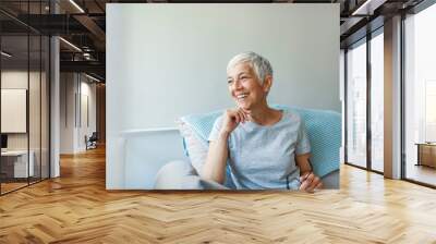 Happy woman relaxing on her couch at home in the sitting room. Portrait of beautiful mature woman smiling while sitting at sofa at home. Beautiful middle age woman smiling at home Wall mural