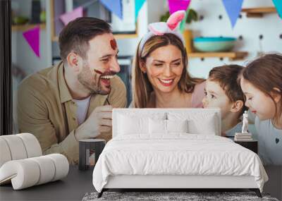 Lovely family prepare for Easter at domestic kitchen. Mother, father, son and daughters are painting eggs. Happy family are preparing for Easter. Cute little child girl and boy wearing bunny ears. Wall mural