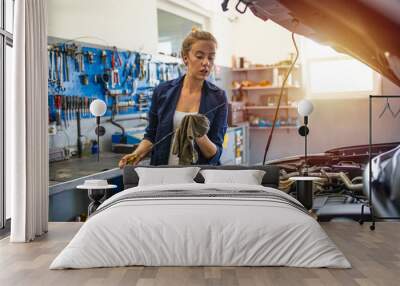 Mechanic working under the hood at the repair garage. Portrait of a happy mechanic woman working on a car in an auto repair shop. Female mechanic working on car Wall mural