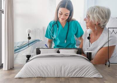 Nurse measuring blood pressure of senior woman at home. Smiling to each other. Wall mural