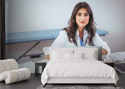 Portrait of female doctor seating in her office at clinic. Friendly Latin American female doctor at the hospital looking at the camera and smiling. Confident female doctor at office desk Wall mural