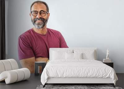 Portrait of happy mature man wearing spectacles and looking at camera indoor. Man with beard and glasses feeling confident.  Handsome mature man posing against a grey background Wall mural