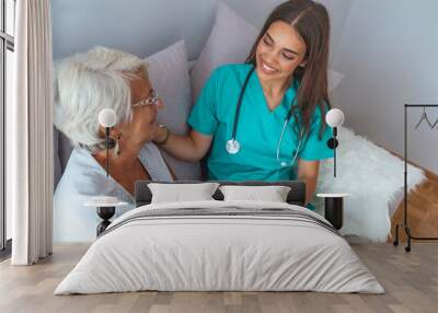 Professional caretaker with her senior charge sitting on a sofa in a bright living room of an assisted living house. Wall mural