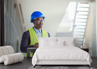 Quality controller in factory. Portrait of smiling engineer in hardhat standing at construction site holding blueprint. Happy male architect writing on clipboard Wall mural