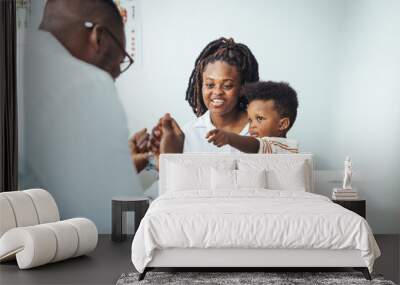 Shot of a single mother bringing his little boy for a checkup. Happy multiracial family visiting clinic for check up. Kind male pediatrician smiles as he talks with an adorable baby boy. Wall mural