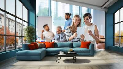 Shot of two businesswomen using a digital tablet together during a collaboration at work.  Female colleagues looking at tablet PC.  Wall mural