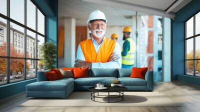 Visiting construction site. Portrait of confident elderly construction engineer in classic suit and hardhat is holding digital tablet and looking at camera while visiting building object Wall mural