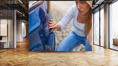 Woman feeling sad after scratching her auto. Frustrated young woman checking pointing at car scratches and dents outdoors during the day, car crash accident, accident insurance. Wall mural