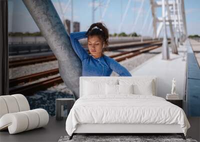 Portrait of a young caucasian beautiful girl in blue sports equipment on the bridge Wall mural