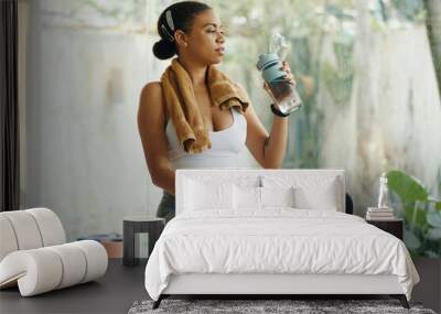 A woman hydrating with a water bottle while sitting on an exercise bike after a workout session Wall mural