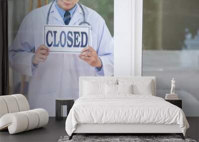 Anonymous guy in medical uniform holding sign with closed writing while standing behind glass in office Wall mural