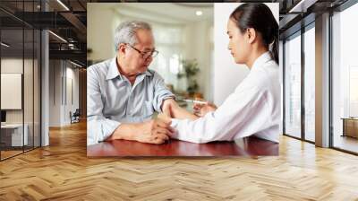 Asian female doctor in white coat making a vaccination from flu to the senior man while they sitting at the table Wall mural