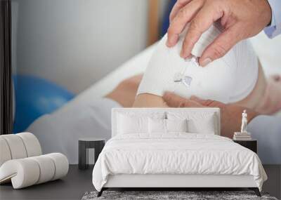 Close-up image of doctor applying elastic bandage on knee Wall mural