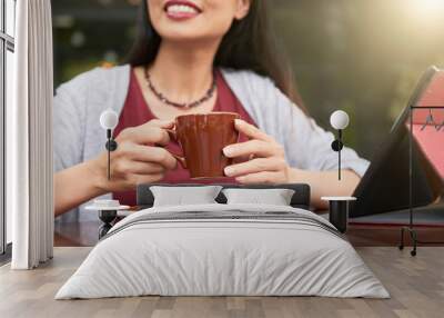 Close-up of smiling young lady sitting at the table with touchpad in front of her and holding cup of coffee Wall mural