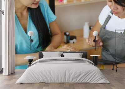 Close-up of two women examining beauty products at modern store. One woman is holding tablet while the other is showing hand for better view Wall mural