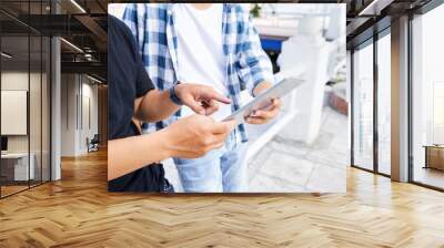 Close-up of two young men standing together with digital tablet and pointing at touchscreen, they communicating online outdoors Wall mural