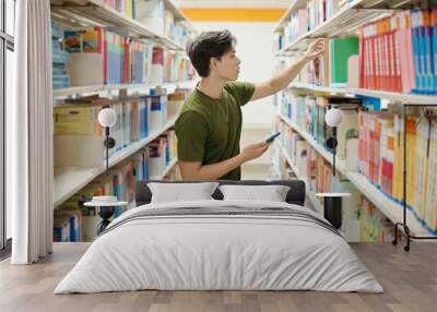 College student with smartphone taking book from shelf Wall mural