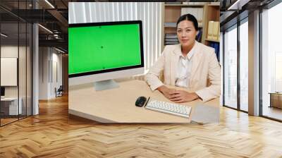 Confident businesswoman sitting at desk showing product presentation on computer Wall mural