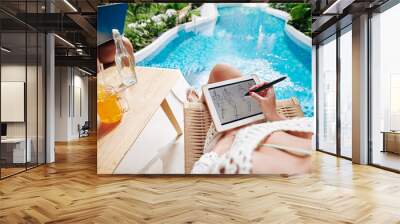 Creative young woman resting by swimming pool, drinking orange cocktail and drawing fashion sketch on tablet computer Wall mural