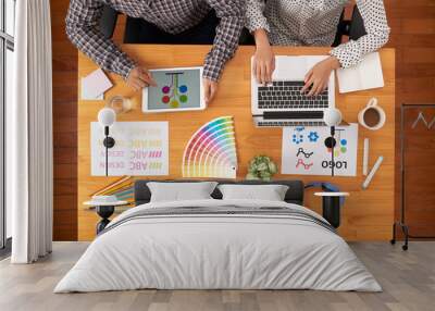 From above shot of two anonymous people in casual outfits sitting at office table and using tablet and laptop while working on design project together Wall mural