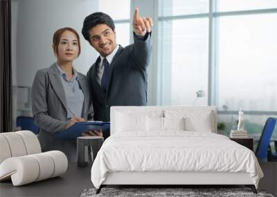 Indian smiling businessman standing at office together with Asian businesswoman and pointing at something Wall mural