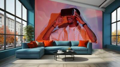 Man wearing virtual reality headset, smiling while holding device. Background illuminated with colorful light patterns, enhancing immersive experience Wall mural