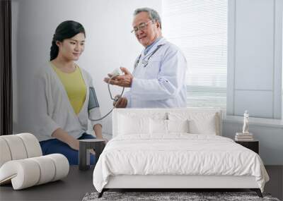 Mature Vietnamese doctor checking blood pressure of young woman Wall mural