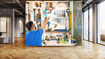 Mechanic taking tool from wall behind his workbench, view from te back Wall mural