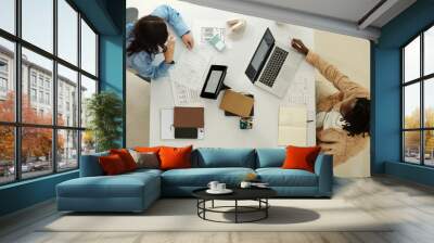 Overhead view of two people at work discussing design ideas at an organized desk with laptops, tablets, and documents showcasing creative brainstorming session Wall mural