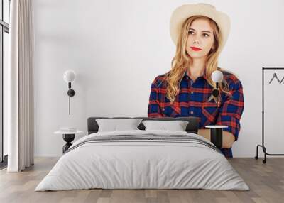 Pensive young woman in plaid shirt and hat crossing arms and looking away Wall mural