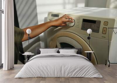 Person adjusting settings on a modern washing machine in bright, well-lit room. Hand turning dial on control panel, showing various options for washing cycle Wall mural