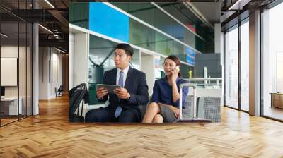 Portrait of Asian man and woman waiting in airport departure zone, using digital devices Wall mural