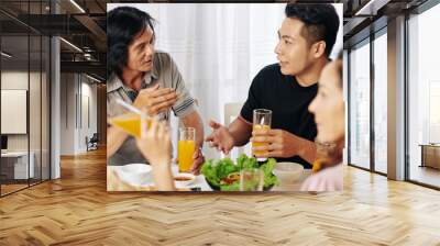 Serious Vietnamese father and adult son talking at family dinner at home Wall mural