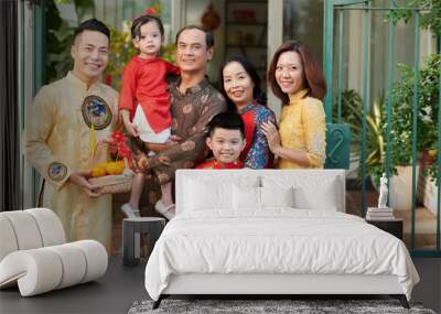 Smiling grandparents, parents and children in traditional ao dai dresses standing in front of house ready for tet celebration Wall mural