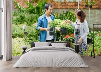 Smiling young gardening center worker offering two blooming plants to mature customer Wall mural