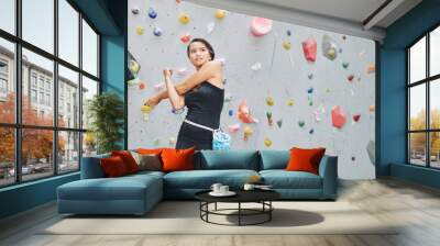 Young Asian woman in black sportswear and with sack of talk on waist warming up hands before climbing wall in gym Wall mural