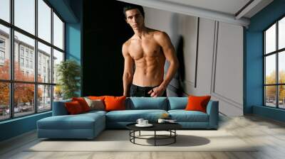 A male model shirtless and suntanned, looking at camera, showing six pack abs, isolated on a grey wall. Wall mural