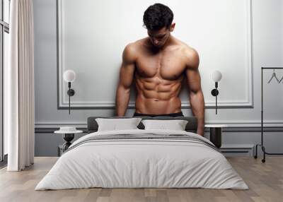 Athlete, muscular man at the white wall poses shirtless, showing six pack abs, white background. Wall mural