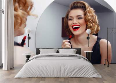 Elegant, smiling young woman, model with charming hairstyle and evening make up, applying red lipstick on sensual lips. Wall mural