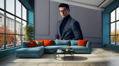 Handsome,fit man in gray suit with black turtleneck,black stylish eyeglasses looks confident at the camera. Wall mural