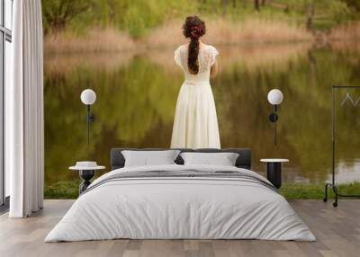 Rear view of a young anonymous bride in a beautiful full wedding dress, with hairstyle, looking down, nature background. Wall mural