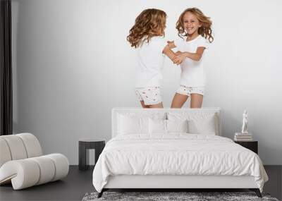 Smiling funny little twin sisters in white clothes dancing isolated on white background children studio portrait. Wall mural