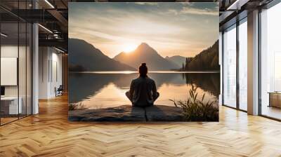 back view of a man sitting in yoga pose in the sundown with a lake and mountains in front of him created by generative AI Wall mural